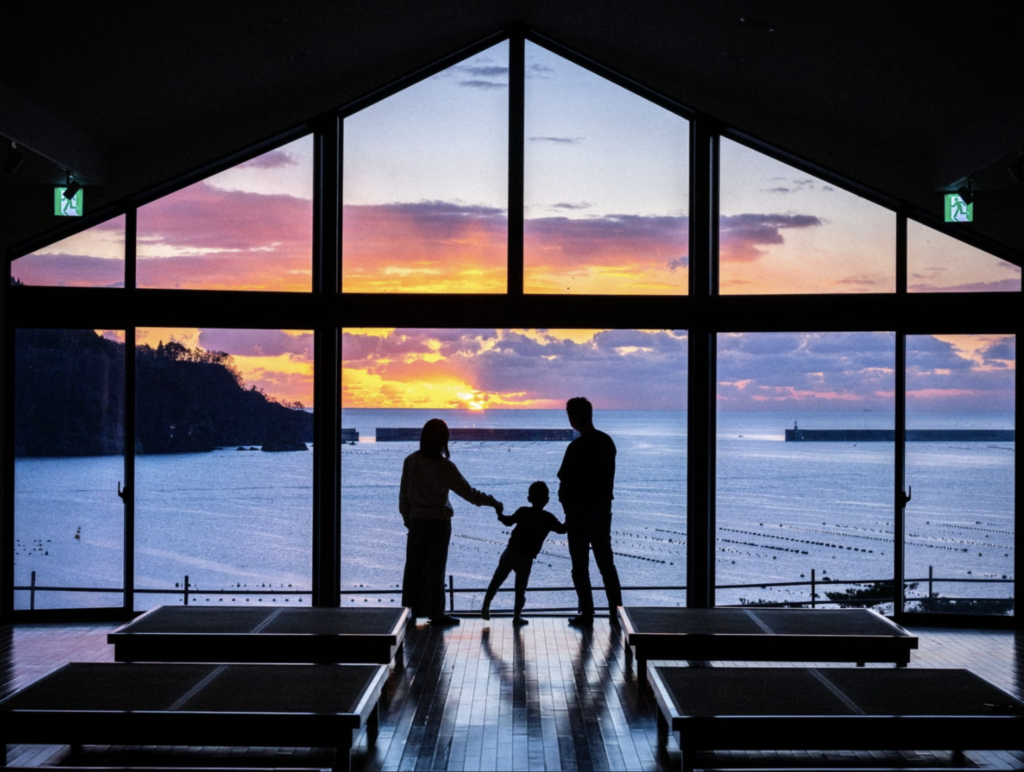 A family captures a serene moment, watching the sun dip below the horizon as waves gently lap the shore at Ofunato Onsen Ryokan.